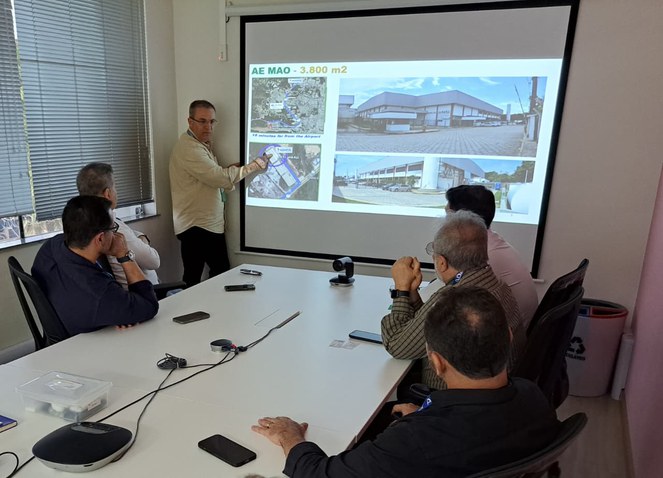 Foto mostra homem em pé fazendo uma explicação com um telão como apoio