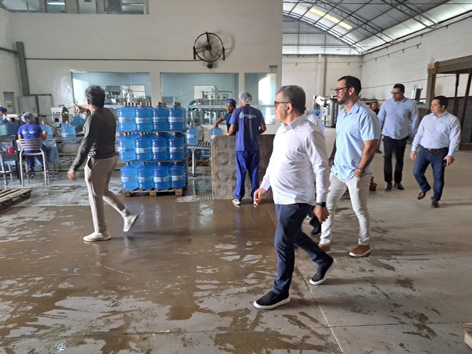Foto mostra homem de branco caminhando com outros homens dentro de uma empresa de água mineral
