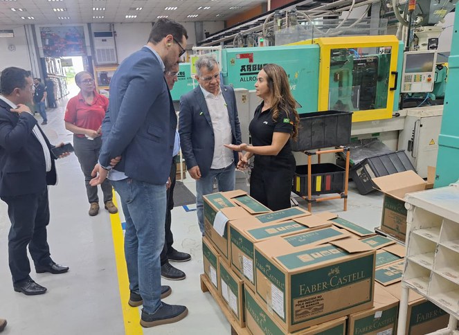 Foto mostra mulher mostrando objeto a grupo de pessoas