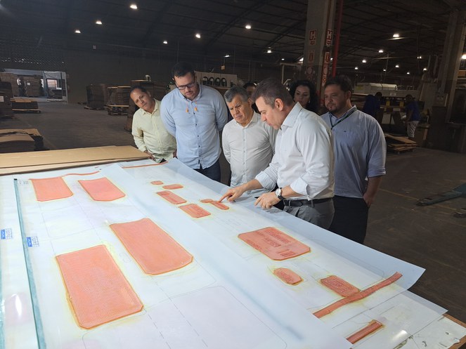 Foto mostra homem de blusa branca mostrando projetos com material de papelão