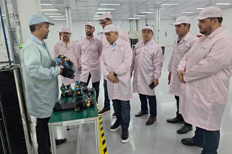 Foto mostra homem segurando um equipamento e mostrando a outros homens, que também estão vestidos de bata