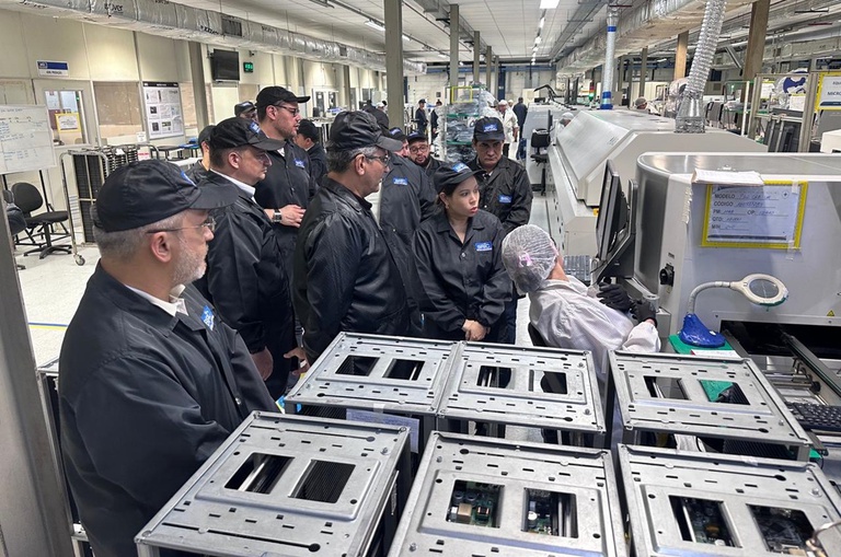 Foto mostra pessoas com jaleco e boné pretos em visita uma fábrica de eleletroeletrônicos