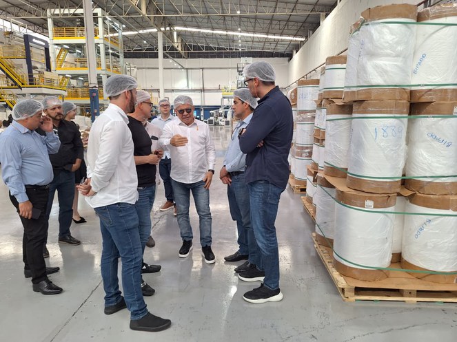 Foto mostra homem de touca branca falando a outros homens em visita a uma fábrica de produtos plásticos