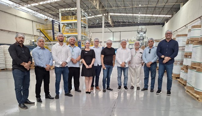 Foto mostra homens de touca branca em uma fábrica de produtos plásticos