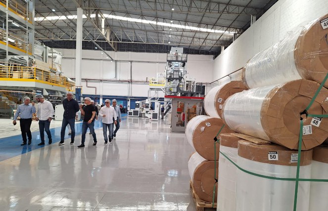 Foto mostra grupo de pessoas de touca branca em visita a uma fábrica de produtos plásticos