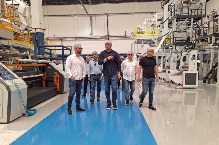 Foto mostra homens de touca branca em visita a uma fábrica de produtos plásticos