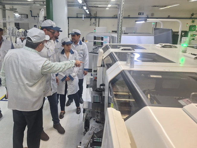 Foto mostra homem mostrando máquinas a grupo de pessoas vestidas com bata e boné brancos