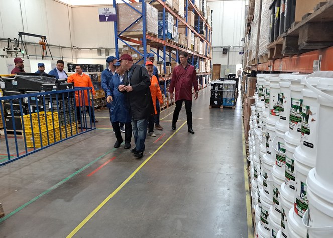 Foto mostra grupo de homens caminhando dentro de uma fábrica de materiais elétricos