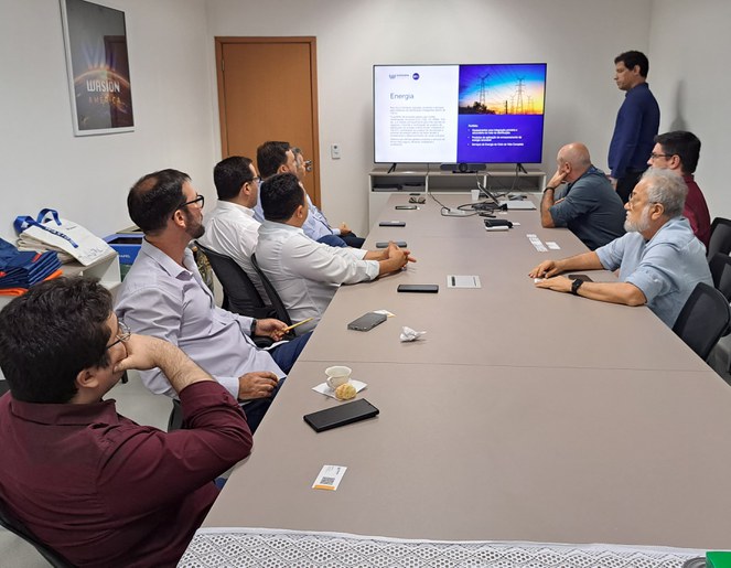 Foto mostra homem em pé e de blusa azul, fazendo uma apresentação a um grupo de outros homens que estão sentados à mesa