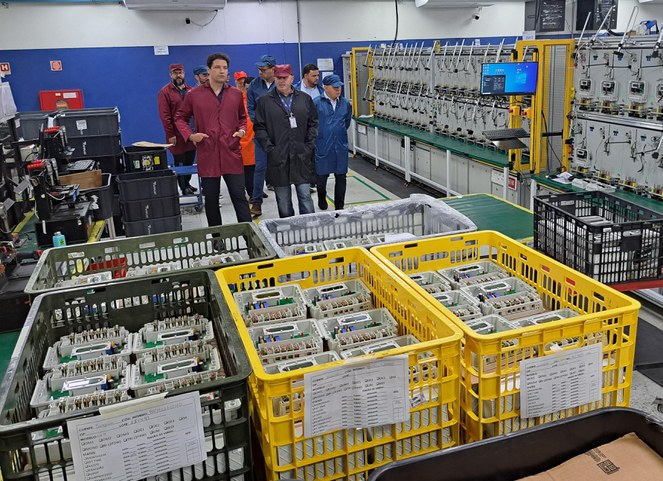 Foto mostra várias caixas com equipamentos elétricos e um grupo de homens observando o material