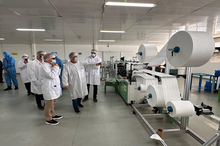 Pessoas diante de uma máquina de produção de máscaras em uma fábrica