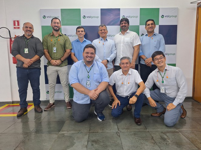 Foto mostra grupo de pessoas posando para fotografia, com um painel e um extintor ao fundo