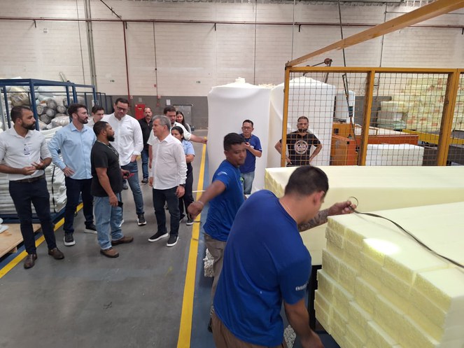 Foto mostra pessoas andando numa fábrica de colchões
