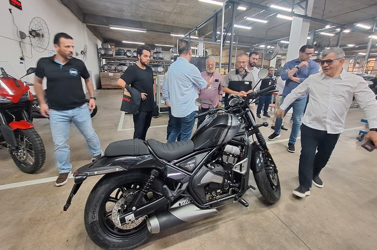 Foto mostra homem de blusa branca observando uma moto