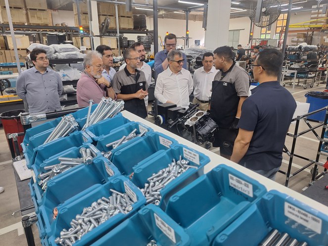 Foto mostra umas caixas com peças de motocicletas e um grupo de pessoas conversando sobre o material