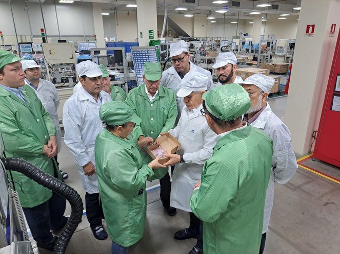 Foto mostra uma mulher vestida de jaleco verde mostrando uma caixa para outro homem de jaleco branco