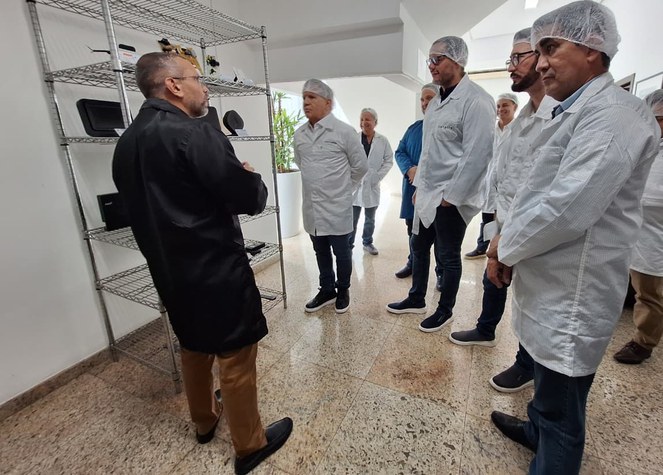 Foto mostra homens de bata em frente a uma estante com produtos eletrônicos