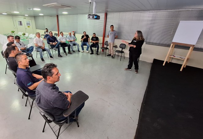 Foto mostra mulher em pé fazendo uma explanação a um grupo de pessoas