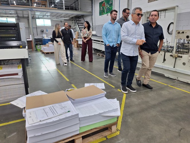 Foto mostra grupo de pessoas caminhando numa fábrica de impressão de papel