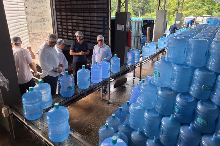 Foto mostra grupo de homens observando garrafões de água