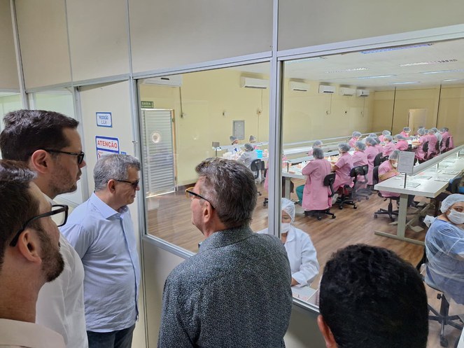 Foto mostra homem de óculos escuros observando grupo de mulheres vestidas de rosa e touca na cabeça