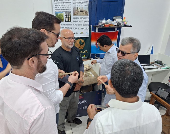 Foto mostra homem de óculos escuros segurando objeto, observado por outros homens