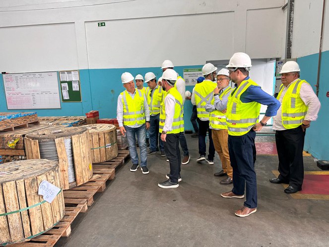 Foto mostra grupo de pessoas com jaqueta verde e capacetes brancos, ao lado de carretéis de cabos de aço