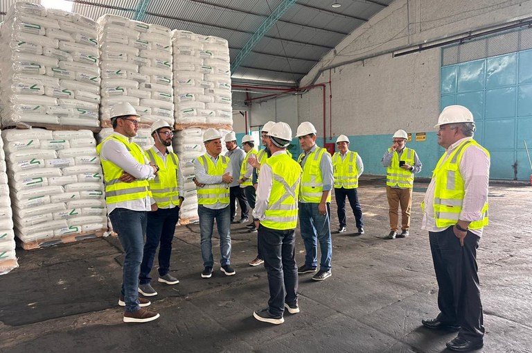 Foto mostra grupo de pessoas usando jaquetas verdes e capacetes, com sacos brancos ao fundo