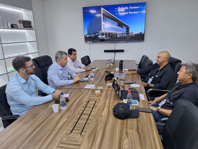 Foto mostra grupo de homens numa reunião, com um telão ao fundo