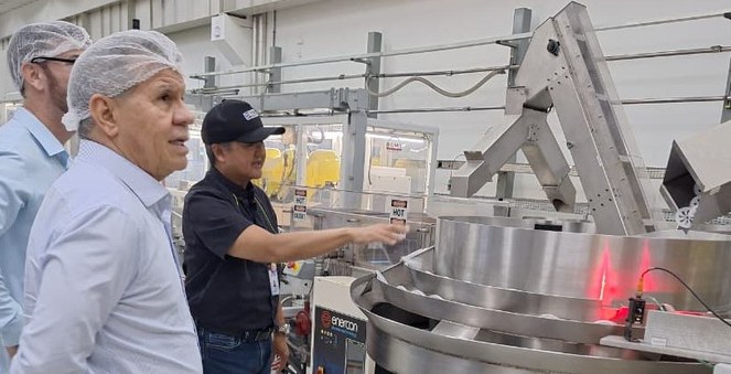 Foto mostra homens acompanhando o funcionamento de uma linha de produção numa fábrica