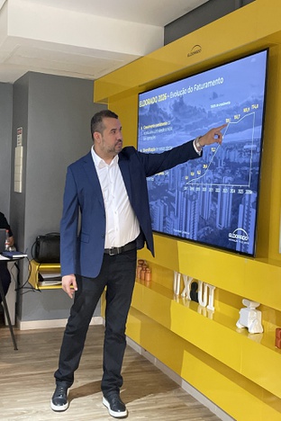 Foto mostra homem de blazer azul apontando para um quadro