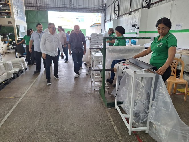 Foto mostra homem de blusa branca andando com um grupo de pessoas em uma fábrica de produtos plásticos