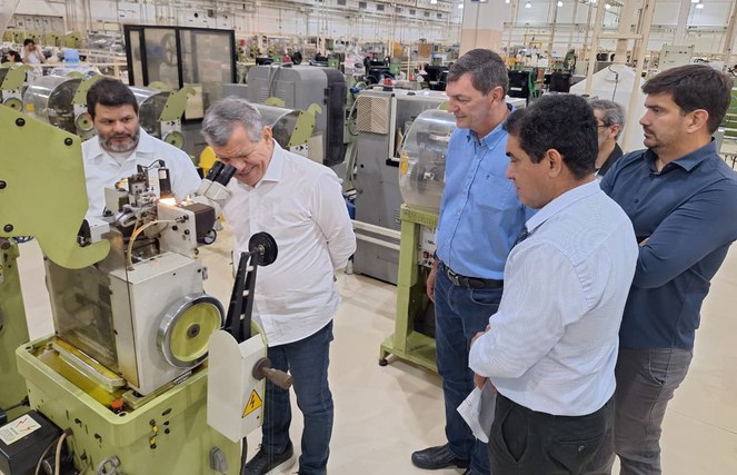 Foto mostra homem olhando num microscópio, observado por outros homens