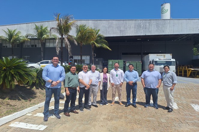 Foto mostra um grupo de pessoas reunidas em frente a uma fábrica
