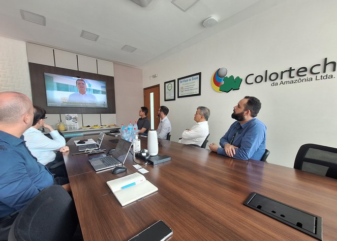 Foto mostra um grupo de pessoas assistindo a uma apresentação num telão