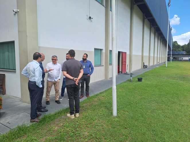 Foto mostra grupo de homens conversando em frente a uma fábrica