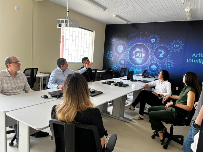 Foto mostra homem apontando para um painel azul, observado por grupo de pessoas