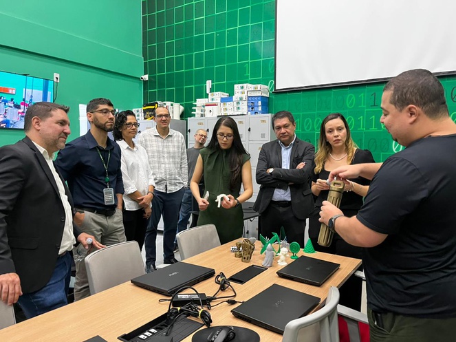 Foto mostra homem manuseando um equipamento observado por grupo de pessoas