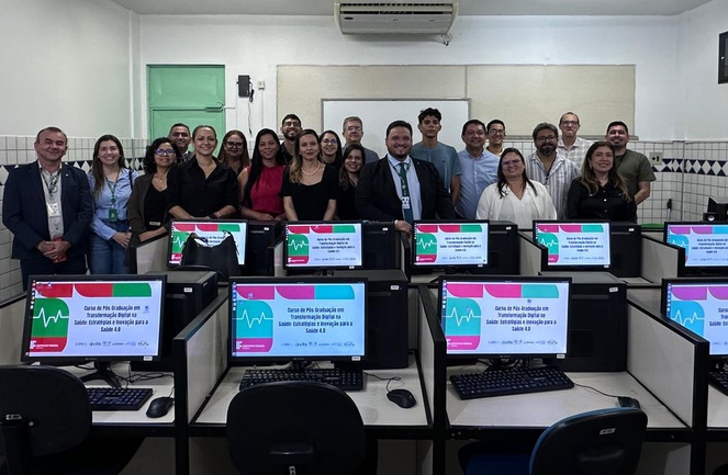 Foto mostra pessoas posando para foto em frente a computadores