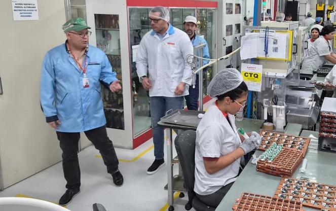 Foto mostra pessoas de bata e toucas em uma linha de produção de equipamentos eletrônicos