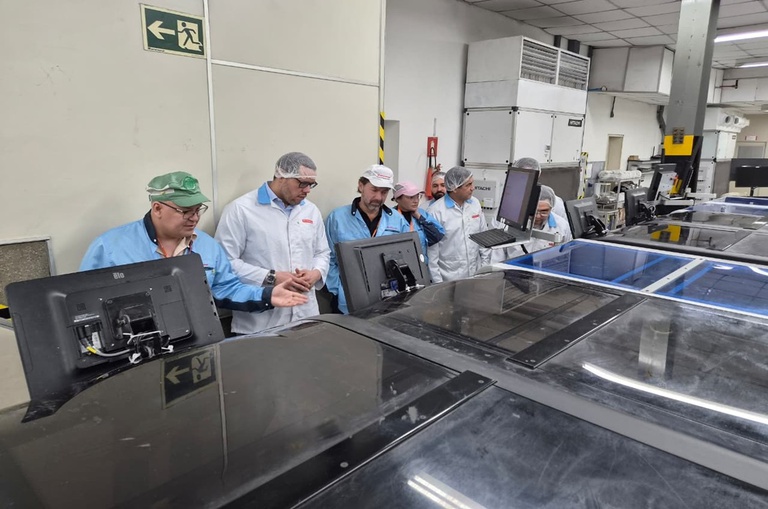 Foto mostra pessoas de bata e toucas em uma linha de produção de equipamentos eletrônicos