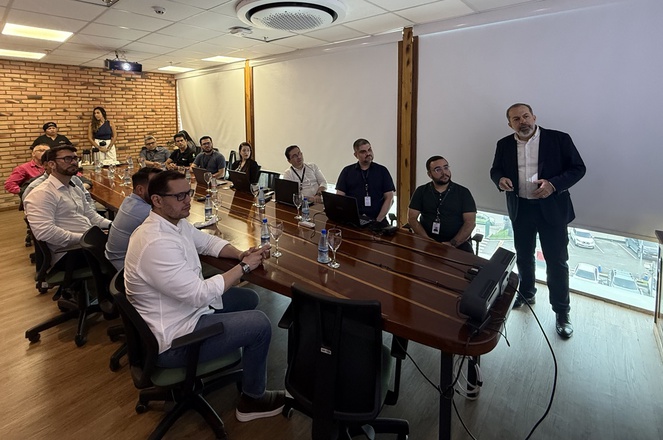 Foto mostra homem de blazer em pé fazendo uma explanação a grupo de pessoas