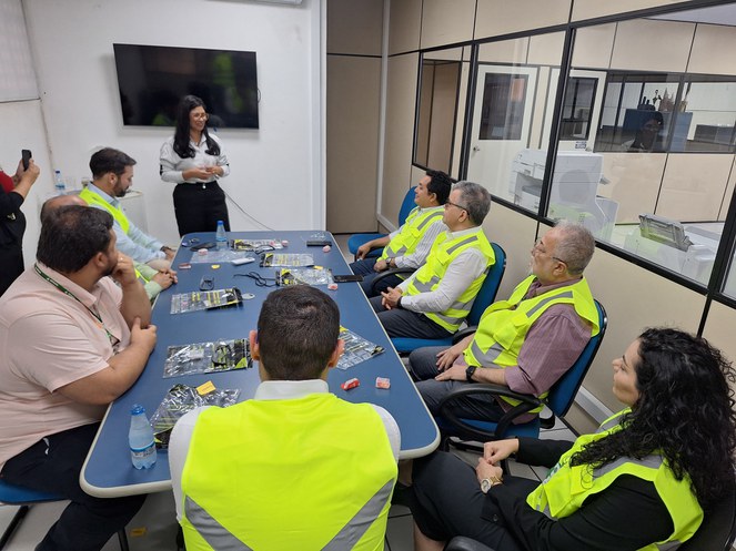 Foto mostra mulher em pé fazendo uma explanação a um grupo de pessoas com jaquetas verdes