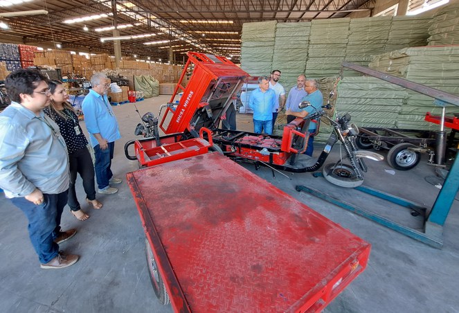 Foto mostra pessoas em uma linha de produção de triciclo elétrico