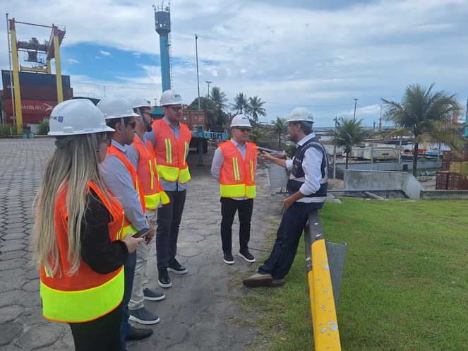 Foto mostra pessoas com capacete branco e contêineres ao fundo, durante visita a um terminal de cargas