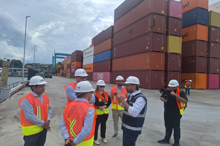 Foto mostra grupo de pessoas com capacete branco e contêineres ao fundo