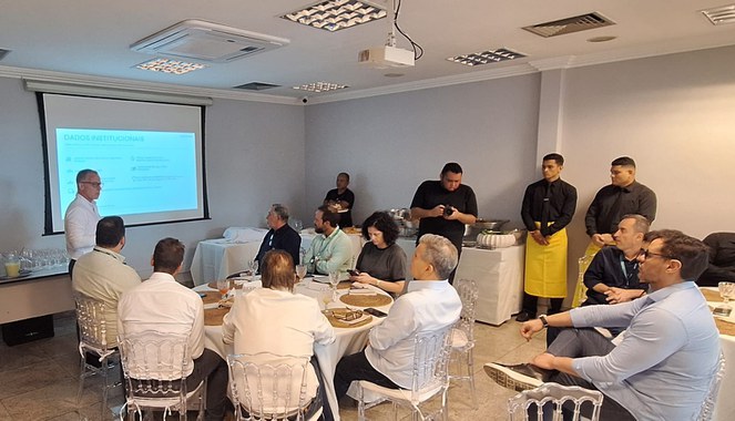 Foto mostra pessoas reunidas ouvindo explicação de um senhor de óculos e blusa branca