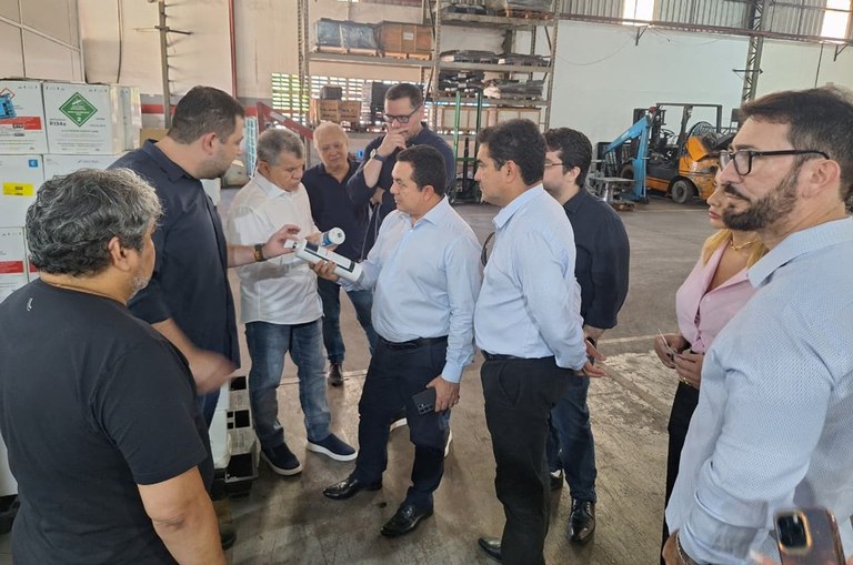 Foto mostra dois homens segurando objetos, observados por outras pessoas