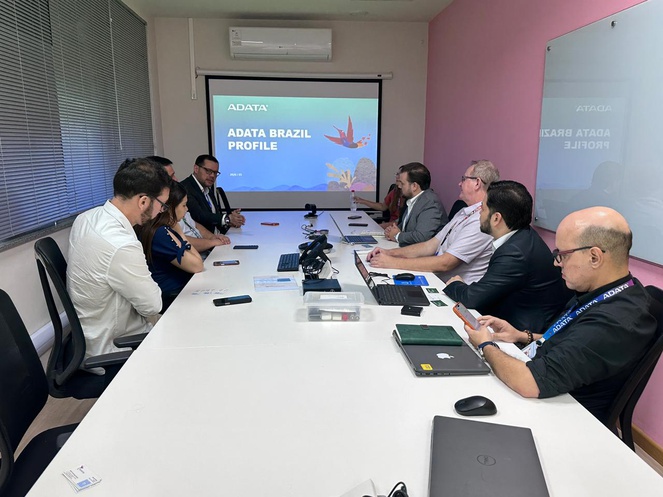 Foto mostra pessoas numa reunião à mesa e com um telão como apoio