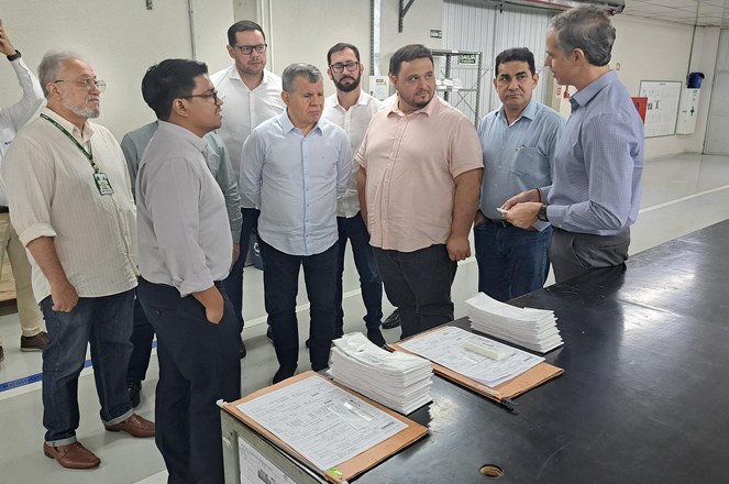 Foto mostra homem de blusa azul falando a outros homens com um papel na mão